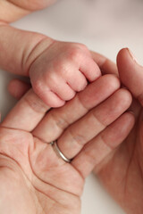 Close-up little hand of child and palm of mother and father. The newborn baby has a firm grip on the parent's finger after birth. A newborn holds on to mom's, dad's finger. 