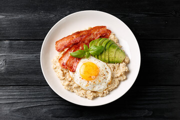 Savory Oatmeal breakfast with sunny side up fried egg, bacon and avocado. Healthy food