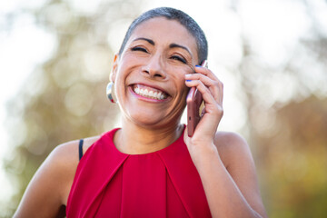 Smiling woman with short hair, wearing a red top, talking on the phone outdoors