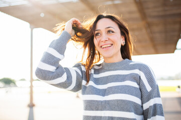 Happy woman in a striped sweater fixing her hair under sunlight outdoors