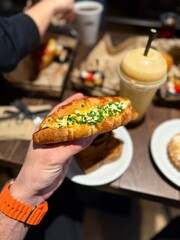 Croissant sandwich with egg holding in hand at cafe shop
