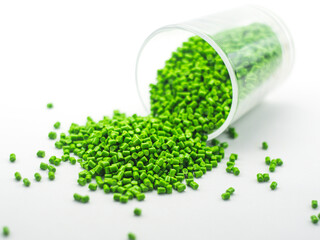 Green masterbatch granules spilling from glass cup,isolated on white background,color pigment...