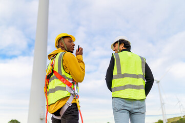 Two engineers wearing safety vests and helmets are discussing using a walkie talkie in a wind...