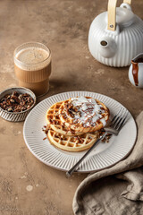 Belgian waffles with vanilla ice cream, nuts and chocolate topping for breakfast on beige textured table background