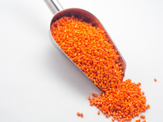 Orange masterbatch granules in stainless steel scoop, isolated on white background. Color pigment...