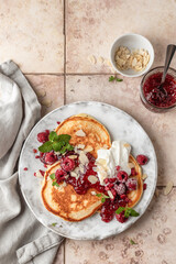Homemade pancakes with yoghurt, berries and raspberry jam. Maslenitsa or Pancake day breakfast on beige tile background, top view