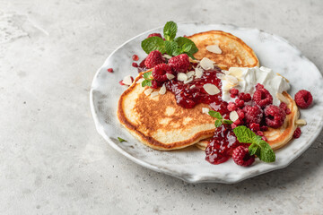 Homemade pancakes with yoghurt, berries and raspberry jam. Maslenitsa or Pancake day breakfast on gray background with text space