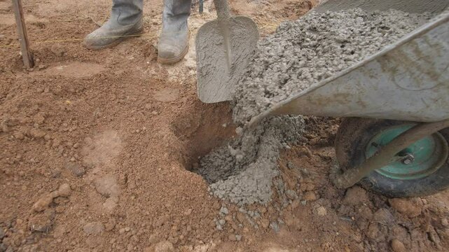 A construction worker skillfully pouring concrete into a prepared hole, essential for building foundation support