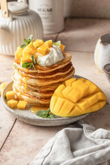 Pancakes with mango, whip cream on top and honey in plate on beige tile background. Delicious dessert for Maslenitsa or Pancake Day. Healthy breakfast