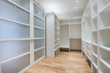 A spacious dressing room with spacious white cabinets and shelves. Sliding door with frosted glass windows.