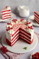 Red Velvet Cake with mascarpone and whipped cream on a plate, decorated with red currant. Pink napkin, grey background and white milk jug. 