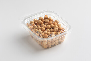 Nuts in a transparent plastic box isolated on white background, close up, food photography, mock up. Pile of shelled hazelnuts in plastic packaging.
