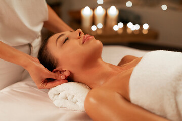 Serene lady client getting ear massage by professional masseuse in spa salon, woman lying in...