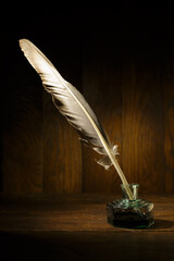Feather and ink bottle on old wooden table. Feather for calligraphy, old education, vintage fonts.