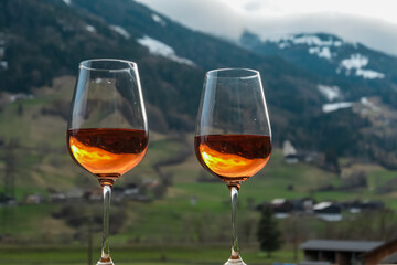 Two glasses of vibrant orange wine stand in sharp focus. Reflections shimmering against a blurred backdrop of the Austrian Alps in Matrei. Moment of relaxation and appreciation. Captured in East Tyrol