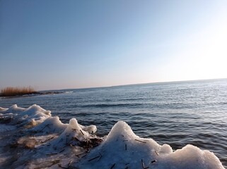 Serene Winter Seascape with Icy Shoreline and Calm Blue Waters, Capturing the Tranquility of a Frozen Beach at Sunset