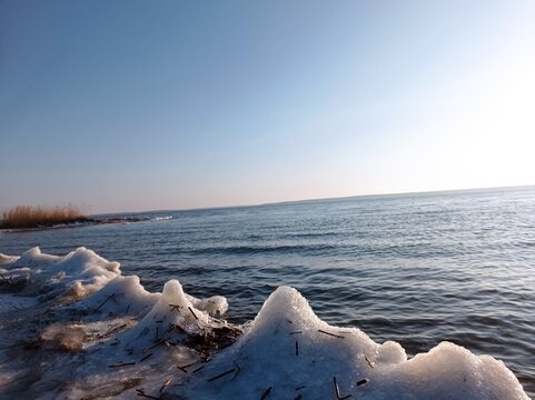 Serene Winter Seascape with Icy Shoreline and Calm Blue Waters, Capturing the Tranquility of a Frozen Beach at Sunset