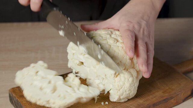 chef cut fresh raw cauliflower on wooden cutting board in a home kitchen for making healthy vegan steaks, food closeup