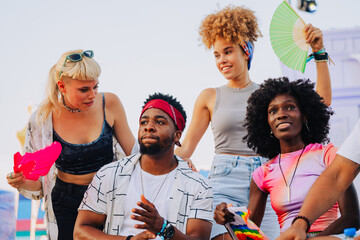Diverse friends enjoying summer music festival, waving colorful fans and holding lgbt flag