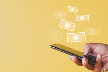E-commerce and fintech concept,hand using smartphone with dollar currency icon floating from screen over yellow background idea for financial technology, mobile payment, and digital wallet innovation.