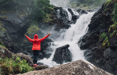 Obraz premium Woman trekker dressed bright red waterproof jacket with enjoying Låtefossen Waterfall, Norway