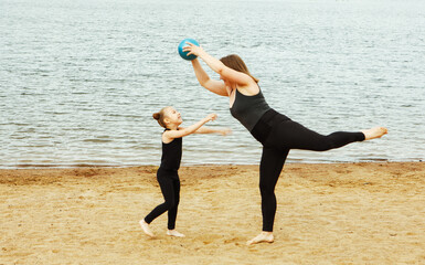 A mother plays ball with her six-year-old daughter on the beach by the lake on a summer day.