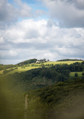 Naklejka premium Forest hilltop with leaf trees and bright green grass field with blue cloudy sky in the background, North Rhine-Westphalia, Germany
