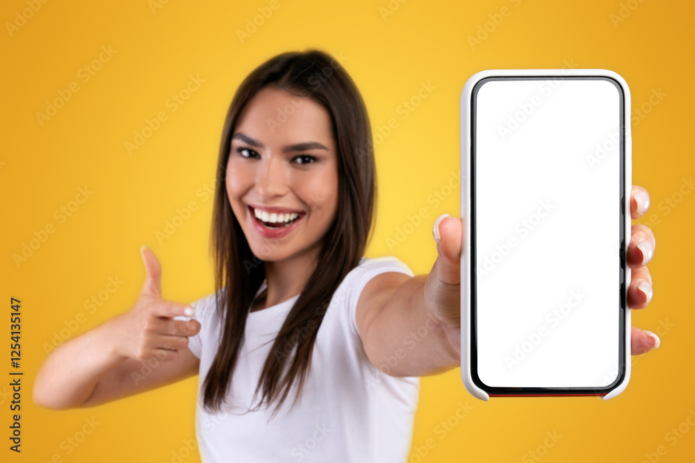 Poster cheerful young lady holding smartphone with white empty screen, pointing at blank display for mobile