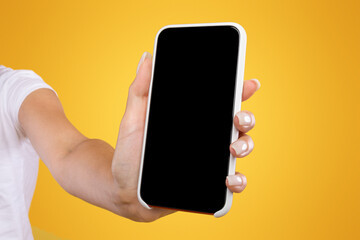 Trendy Mobile Phone. Closeup of female holding smartphone with black empty screen in hand, showing device close to camera. Gadget with blank space, mock up, selective focus, orange blurred background