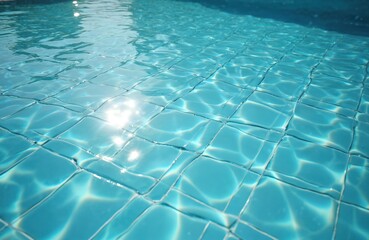 Crystal clear blue water in swimming pool. Light reflects creating wave pattern on tiles floor. Relaxing summertime vibe, aquatic background for wellness, holidays, vacation.