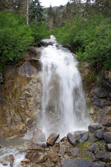 Fototapeta premium A mesmerizing waterfall flowing over rugged rocks, surrounded by lush greenery and towering trees in the Alaskan wilderness near Skagway. 
