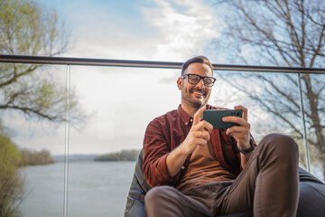 Adult man with eyeglasses play video games on his phone at home