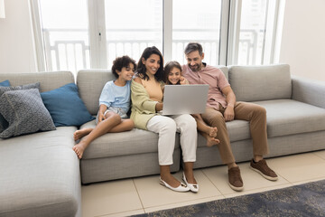 Obraz premium Family with children spend leisure with laptop, settled woman comfortable on cozy couch watching movie via online digital subscription services, buying goods, making order through internet. Tech usage