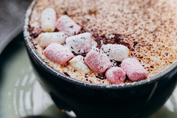 Cup of hot chocolate with marshmallows and cocoa powder on a rustic dark background