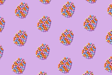 Colorful easter dragee on a violet background. Multicolored candies in the shape of eggs covered with glaze