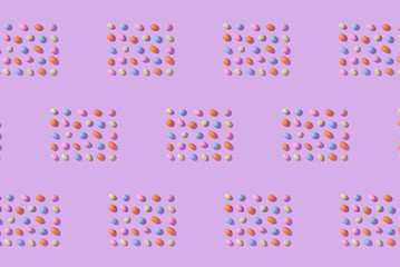 Colorful easter dragee on a violet background. Multicolored candies in the shape of eggs covered with glaze