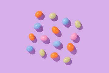 Colorful easter dragee on a violet background. Multicolored candies in the shape of eggs covered with glaze