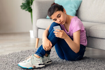 Unhappy Indian teen girl with mobile phone feeling lonely and sad, suffering from cyber bullying...