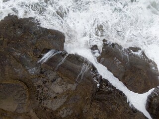 Naklejka premium Powerful waves crash against rugged coastal rocks. Ocean spray creates a foamy white line. Coastal erosion. Piha, Auckland, New Zealand