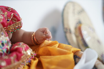 A baby dressed in traditional attire with gold bangles, against a backdrop of woven baskets. A heartwarming and cultural portrait symbolizing heritage, festivities, and cherished traditions.