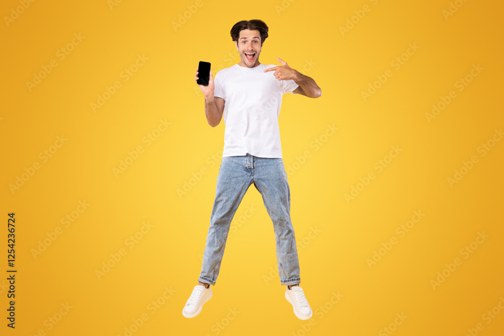 Poster cool mobile app. excited casual guy pointing finger at smartphone with blank screen and jumping up o