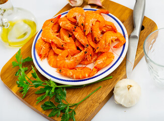 Whole raw red prawns with olive oil, cloves of garlic and fresh greens on plate. Popular seafood delicacies..
