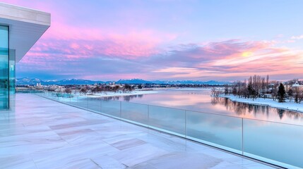 Fototapeta premium Modern glass balcony overlooking a calm river and snowy mountains during a vibrant pink sunset.