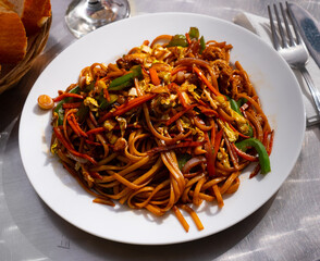 Fried noodles with vegetables and bread served on a white plate in a cafe