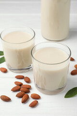 Fresh nut milk, green leaves and almonds on white wooden table, closeup