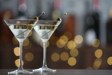Martini cocktail with olives in glasses on wooden table against blurred background, closeup. Bokeh effect