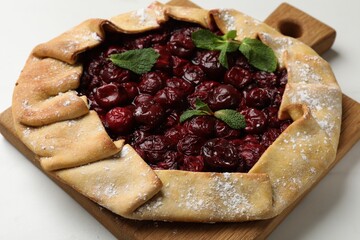 Tasty galette with cherries and mint on white table, closeup