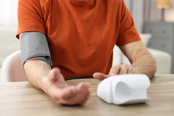 Senior man measuring blood pressure at table indoors, closeup