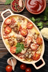 Delicious pasta casserole in baking dish with ingredients and sauce on wooden table, flat lay