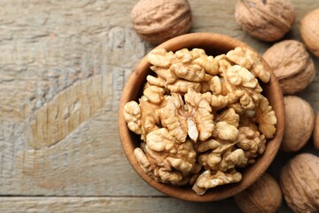 Peeled walnuts in bowl and whole ones on wooden table, flat lay. Space for text